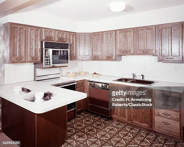 Modern, fitted kitchen with linoleum flooring, cabinets in a dark wood finish, a dining counter island and appliances including a stove and microwave...