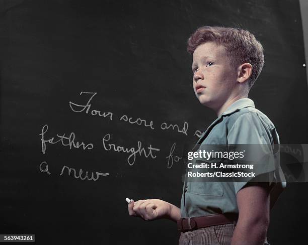 1950s FRECKLE FACED RED HAIRED BOY AT BLACKBOARD WRITING WITH CHALK GETTYSBURG ADDRESS SCHOOL HISTORY CLASS FOUR SCORE