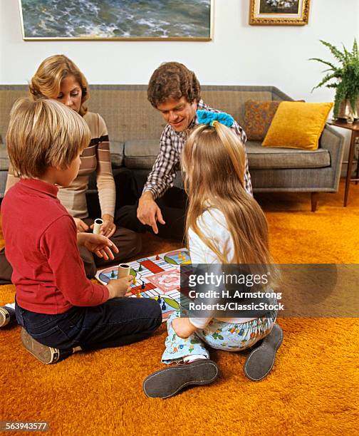 1970s FAMILY MOTHER FATHER SON DAUGHTER PLAYING BOARD GAME IN LIVING ROOM SITTING ON FLOOR SHAG CARPET