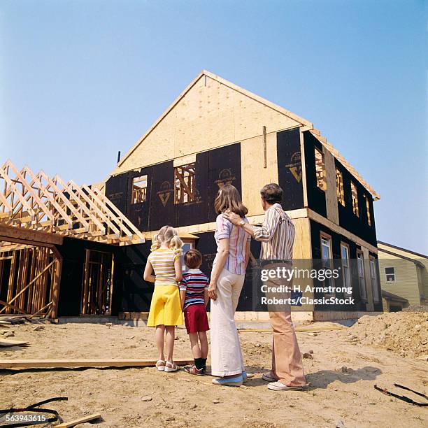 1970s FAMILY OF FOUR MAN WOMAN BOY GIRL LOOKING AT NEW HOME UNDER CONSTRUCTION