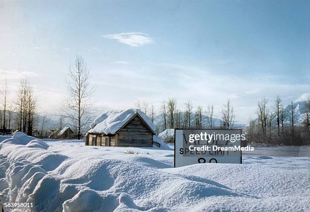 1950s LOG CABIN BUILDING DEEP WINTER SNOW OBSCURES SPEED LIMIT SIGN VALDEZ ALASKA USA