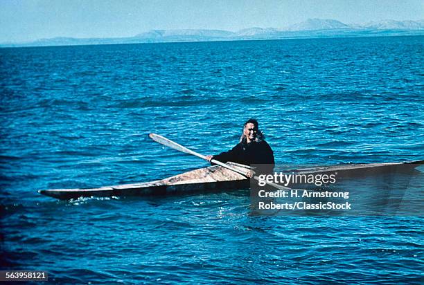 1960s SMILING INUK MAN LOOKING AT CAMERA PADDLING SKIN KAYAK IN ARCTIC OCEAN KOTZEBUE ALASKA USA