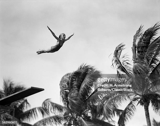 1930s GIRL IN MID AIR DIVING INTO SWIMMING POOL PALM TREES IN BACKGROUND