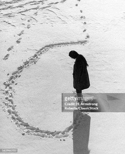 1970s OVERHEAD VIEW OF ANONYMOUS SILHOUETTED WOMAN MAKING CIRCULAR TRACKS IN WINTER SNOW OUTDOOR