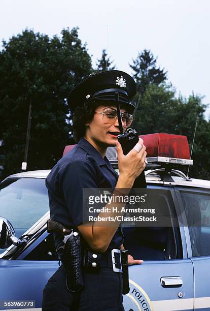 1970s POLICE WOMAN TALKS ON WALKIE TALKIE IN FROMT OF POLICE CAR