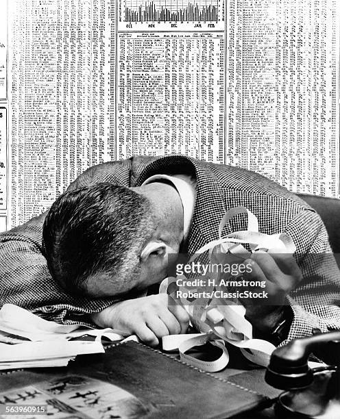 1940s MAN HEAD ON DESK HOLDING STOCK TICKER TAPE WITH NEWSPAPER STOCK PAGE BEHIND HIM