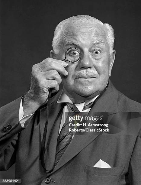 1950s 1960s SURPRISED SENIOR BUSINESSMAN MAN LOOKING AT CAMERA THROUGH MONOCLE WITH FUNNY ALARMED FACIAL EXPRESSION