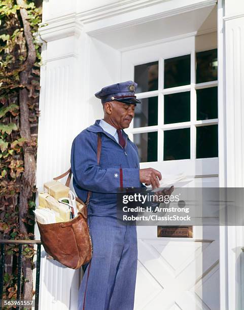1960s UNIFORMED AFRICAN AMERICAN MAILMAN CARRYING LEATHER MAILBAG SORTING AND DELIVERING LETTERS TO FRONT DOOR