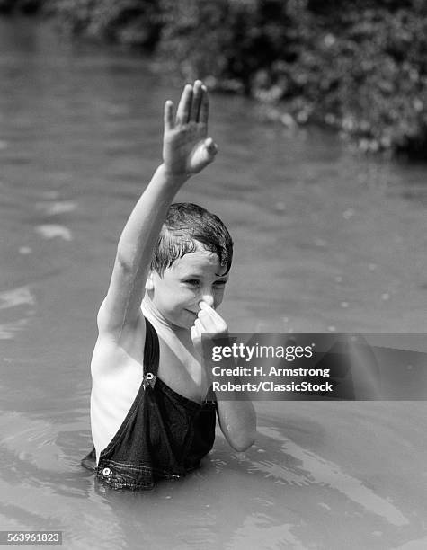 1930s BOY WEARING OVERALLS AS BATHING SUIT STANDING IN CREEK ARM UP & HOLDING NOSE TO GO UNDERWATER