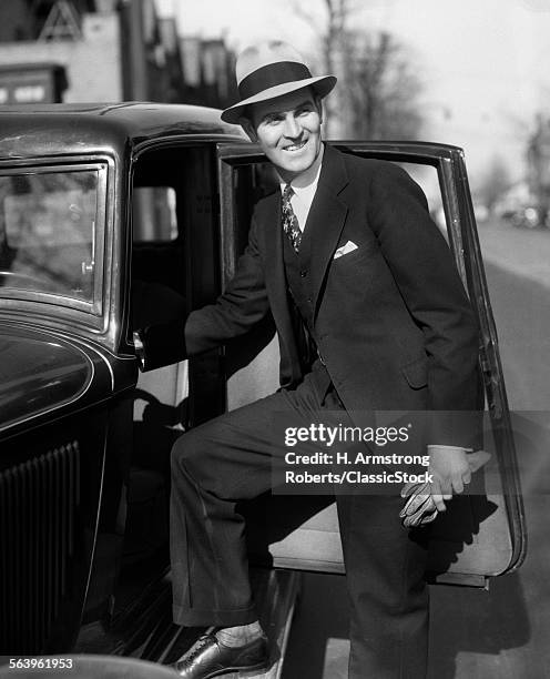 1930s SMILING MAN IN SUIT AND HAT HOLDING GLOVES STEPPING INTO AUTOMOBILE DRIVER SEAT