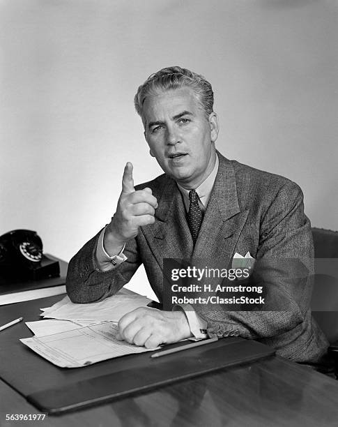 1940s BUSINESSMAN SITTING AT DESK SPEAKING SHAKING FINGER AND LOOKING AT CAMERA MAKING A POINT