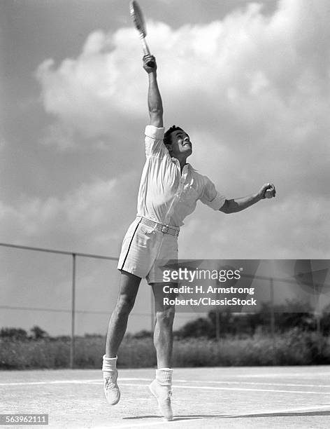 1930s MAN IN MID SERVE PLAYING TENNIS JUMPING SWINGING TENNIS RACKET TO HIT BALL