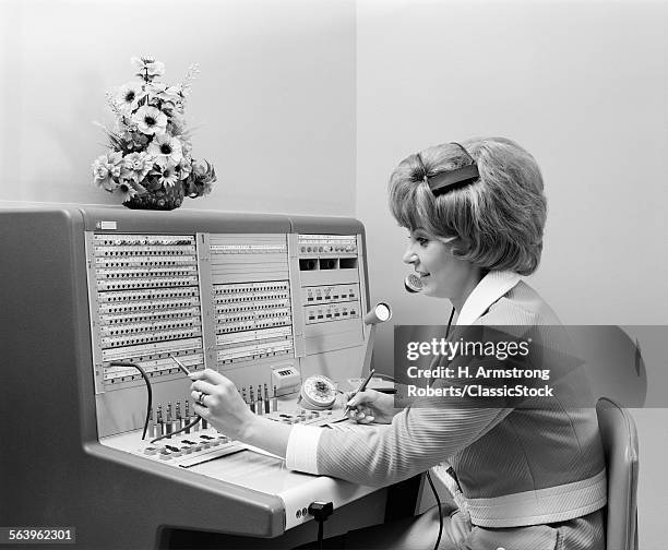 1970s SMILING WOMAN OPERATOR RECEPTIONIST WORKING ANSWERING OFFICE TELEPHONE SWITCHBOARD WEARING HEADSET INDOOR