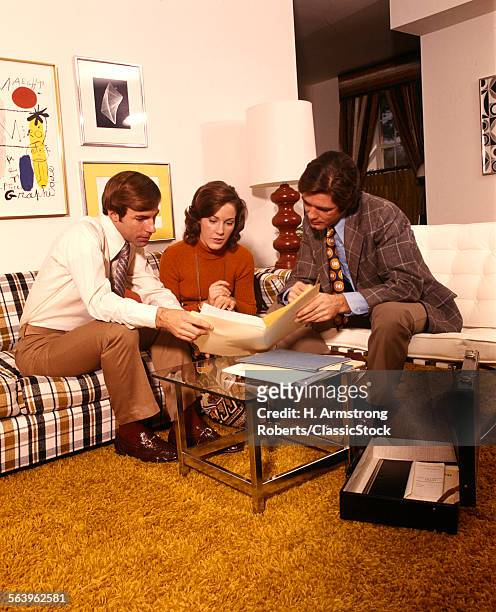 1970s MAN WOMAN HUSBAND WIFE ON COUCH IN LIVING ROOM TALKING TO SALESMAN READING CONTRACT INSURANCE SALES SHAG CARPET