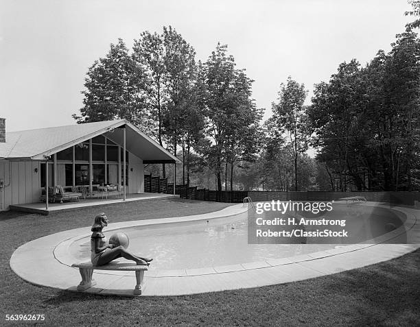 1950s 1960s BLOND WOMAN BATHING SUIT SITTING ON STONE BENCH BEACH BALL NEAR KIDNEY SHAPED SWIMMING POOL