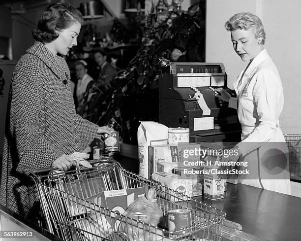 1950s WOMAN AT GROCERY STORE CHECKOUT COUNTER HANDING ITEMS OVER FOR CASHIER TO RING UP ON CASH REGISTER