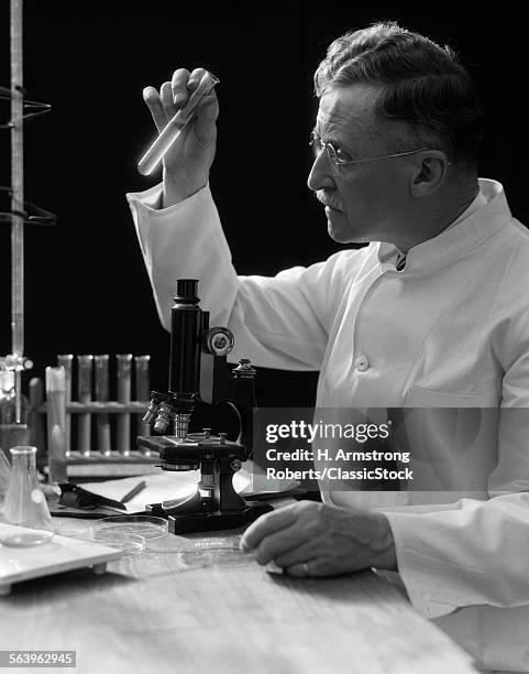 1920s 1930s 1940s SCIENTIST LAB TECHNICIAN IN WHITE COAT LOOKING AT TEST-TUBE IN FRONT OF MICROSCOPE