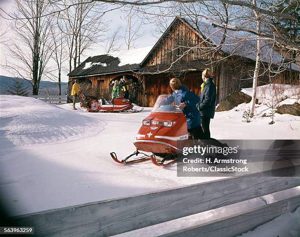 1960s 1970s PEOPLE IN SNOWMOBILES SNOW VEHICLE OUTSIDE RURAL CABIN SEVERAL WOMEN MEN