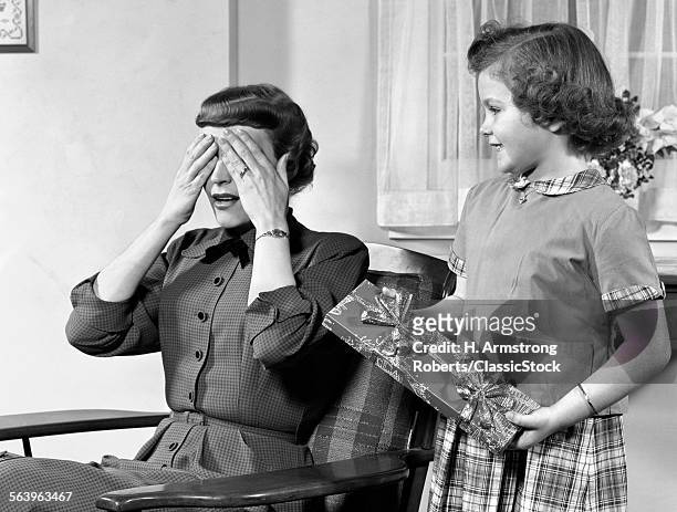 1950s WOMAN MOTHER HANDS COVERING EYES AS GIRL DAUGHTER GIVES HER A GIFT PRESENT