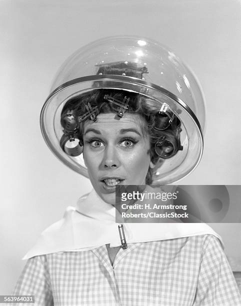 1960s PORTRAIT OF WOMAN IN CURLERS UNDER HAIR DRYER