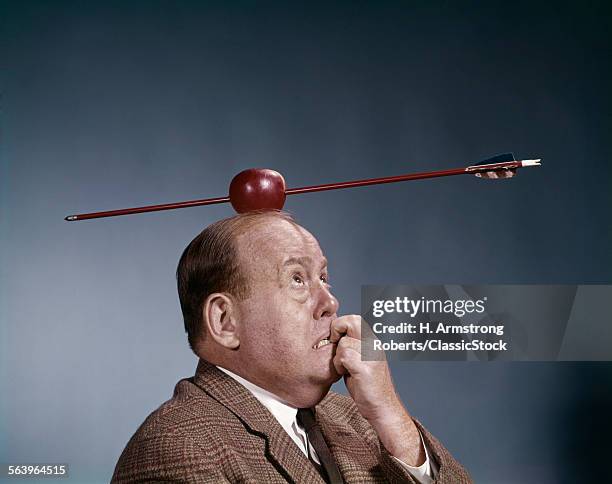 1960s ANXIOUS BUSINESS MAN BITING FINGER NAILS ARROW SHOT THROUGH APPLE TOP HEAD WILLIAM TELL SYMBOL