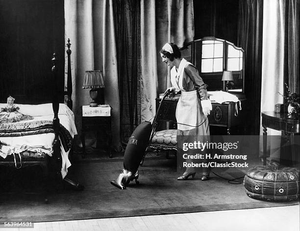 1920s UNIFORMED MAID RUNNING EUREKA VACUUM IN BEDROOM