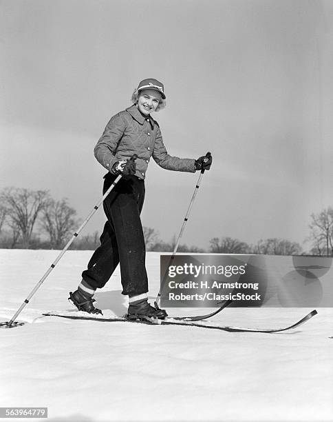 1940s 1950s WOMAN SMILING LOOKING AT CAMERA ON WOOD SKIS WITH BAMBOO SKI POLE IN EACH HAND WEARING QUILTED JACKET