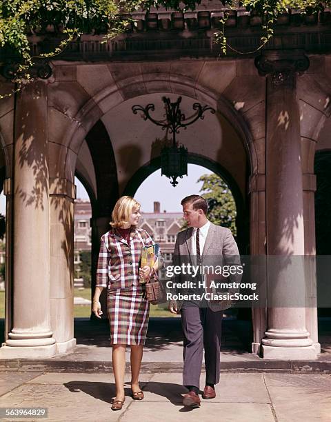 1960s MAN AND WOMAN STUDENTS WITH BOOKS AT ARCH LEADING TO CAMPUS QUADRANGLE