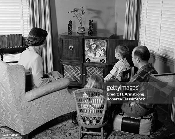 1950s BACK VIEW OF FAMILY OF 4 GATHERED AROUND TV SET WATCHING CLOWN WITH BALLOONS