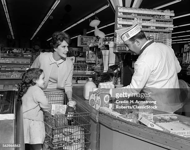 1960s MOTHER DAUGHTER UNLOAD GROCERY CART AT SUPERMARKET CHECKOUT COUNTER MAN CLERK CASHIER RINGS UP CASH REGISTER