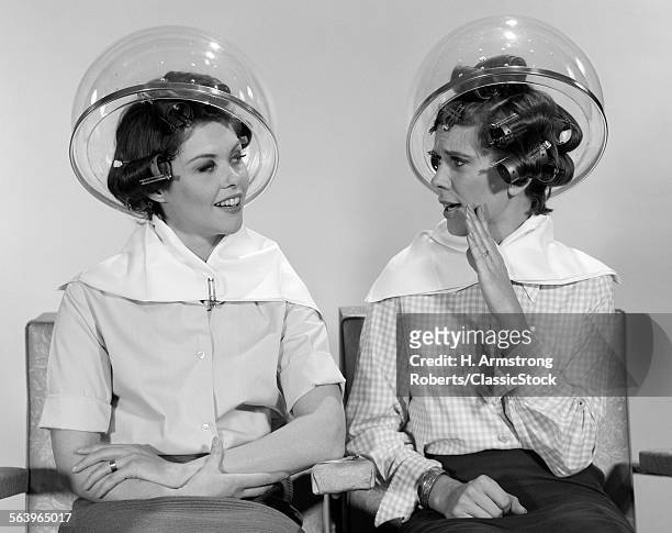 1960s TWO WOMEN SITTING TOGETHER GOSSIPING UNDER HAIRDRESSER HAIR DRYER