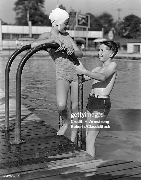 1930s 1940s GIRL AND BOY STANDING ON POOL LADDER WEARING BATHING SUITS