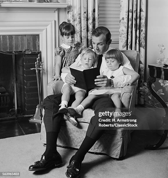 41970s MAN FATHER SITTING IN CHAIR WITH THREE CHILDREN READING BOOK