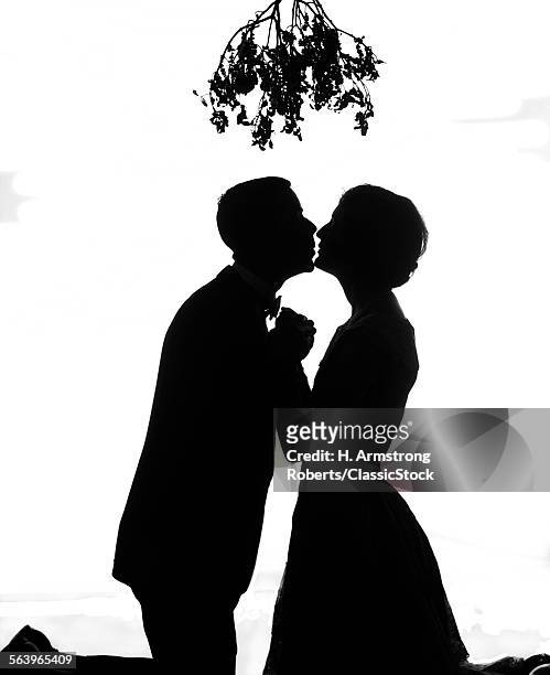 1920s SILHOUETTE OF ANONYMOUS COUPLE HOLDING HANDS KISSING UNDER CHRISTMAS MISTLETOE
