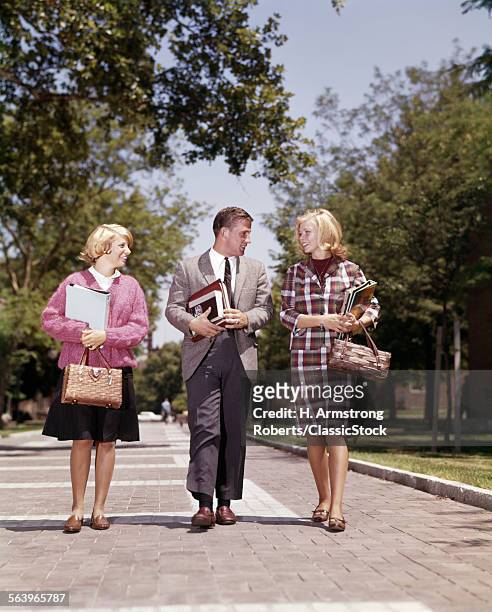 1960s 3 STUDENTS WALKING ON CAMPUS CARRY BOOKS BOY IN SUIT & TIE TWO BLONDE GIRLS STRAW HAND BAGS FASHION BRICK SIDEWALK
