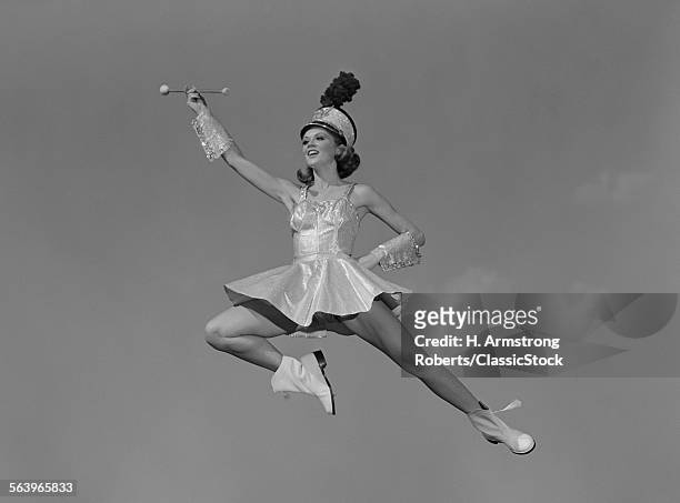 1960s WOMAN MAJORETTE HOLDING BATON WEARING SHORT SKIRT UNIFORM JUMPING INTO THE AIR