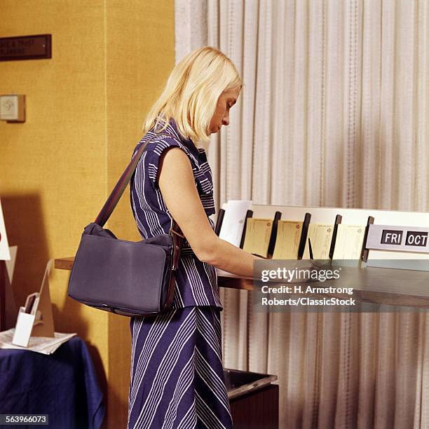 1970s BLONDE WOMAN WRITING A DEPOSIT SLIP AT COUNTER IN BANK