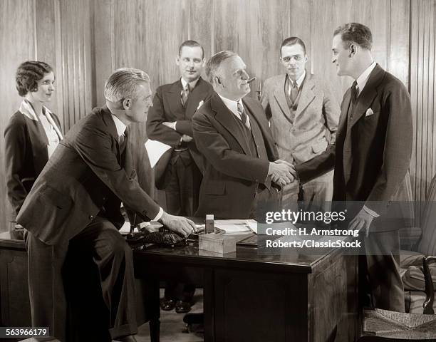 1930s GROUP BUSINESS MEN AND WOMAN IN OFFICE BOSS SHAKING HANDS WITH NEW HIRE