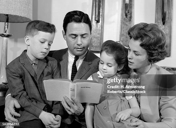 1960s FAMILY MOTHER FATHER SON DAUGHTER SITTING TOGETHER READING BIBLE INDOOR