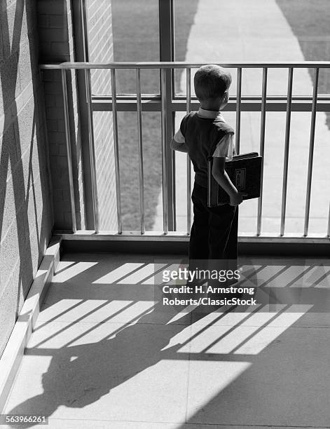 1950s ANONYMOUS SILHOUETTED SCHOOLBOY WITH BOOKS UNDER ARM LOOKING OUT WINDOW BETWEEN BARS OF RAILING SHADOW CAST BEHIND HIM