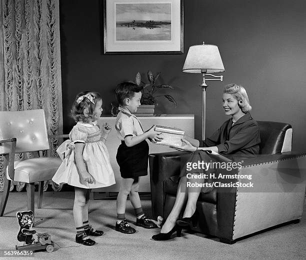 1950s LITTLE BOY AND GIRL SON AND DAUGHTER GIVING WOMAN MOTHER SITTING IN LIVING ROOM A GIFT PRESENT