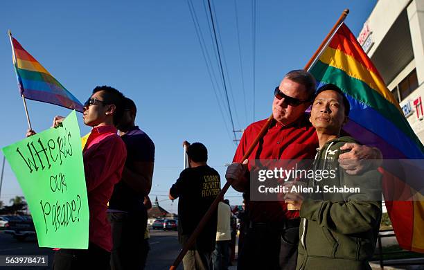 Minh Tran, left, of Westminster, holds a sign and gay pride flag, and Bob Tucker, in red shirt, hugs his partner, Quan Nguyen, right, both of Garden...