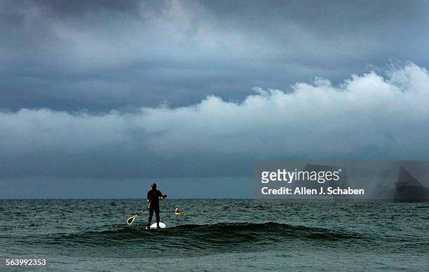 Paddle surfer Robert Franklin of Huntington Beach, looks to a stormy skyline as he waits for a wave to roll in as waves increase in size near the...