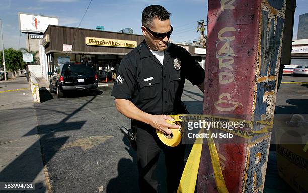 Los Angeles police officer Vic Gutierrez uses crime scene tape to contain the scene of a homocide in the Westlake/Koreatown area. From Jill Leovy...