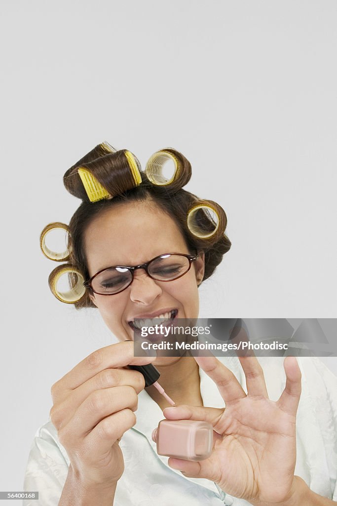 Smiling young woman in curlers polishing her fingernails