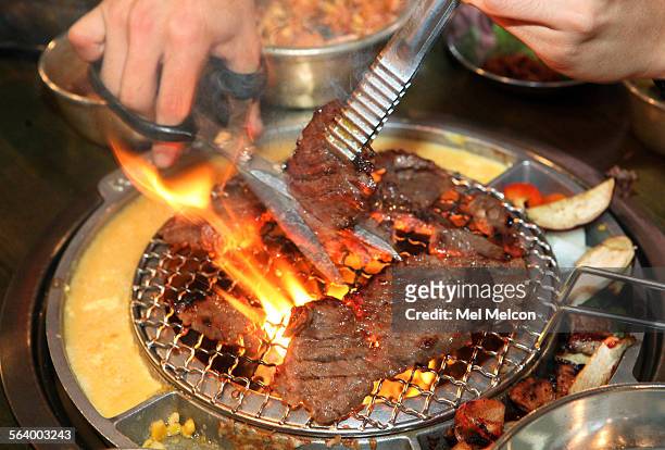Patron cuts portions of galbi beef into smaller pieces, as it cooks on a burner at his table inside the Korean BBQ restaruant, Kang Ho Dong Baekjong,...