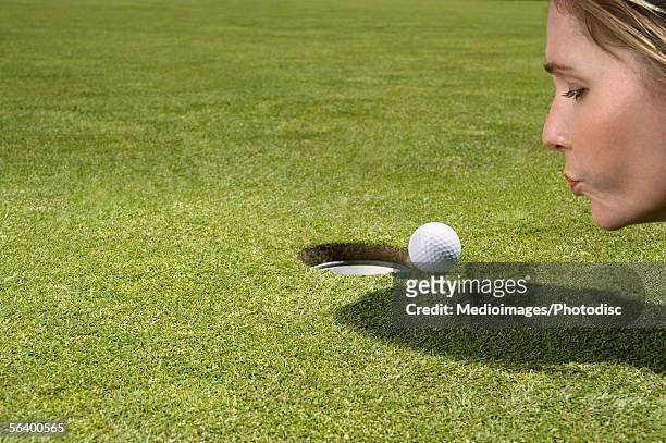 woman blowing on golf ball near hole - golf cheating imagens e fotografias de stock