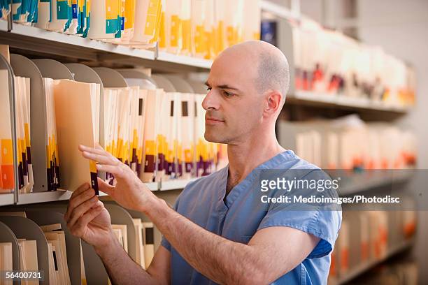 male doctor reading file in medical records room - filing cabinet stock pictures, royalty-free photos & images