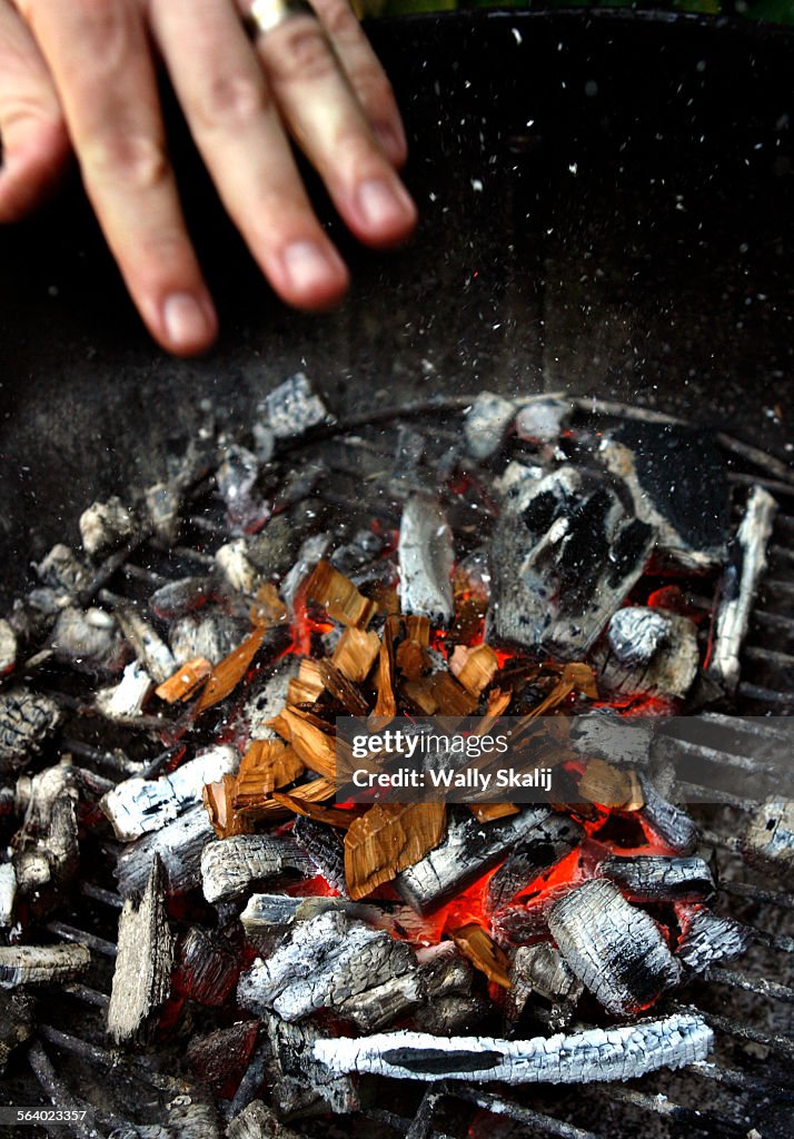 Sprinkling presoaked wood chips on the charcoal.