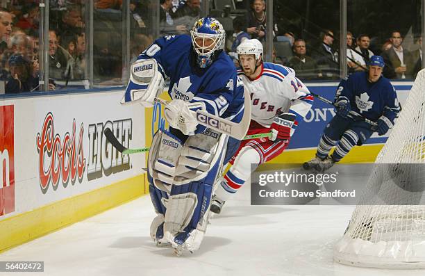 Goaltender Ed Belfour of the Toronto Maple Leafs plays the puck behind the net as Jason Ward of the New York Rangers pressures him during their NHL...